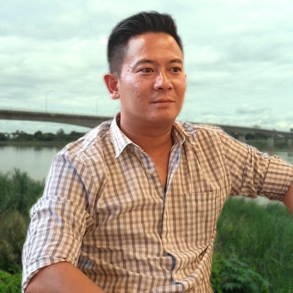 Atjawin (Up) in a gray checked shirt, with the Thai-Lao Friendship Bridge over the Mekong in Nong Khai behind him